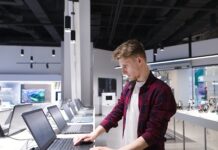 Apple vs. Lenovo: Which Brand Is Better? A young man chooses a laptop in an electronics store. A man looks at laptops in the computer department at the technology store. Buy a laptop