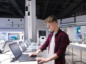 A young man chooses a laptop in an electronics store. A man looks at laptops in the computer department at the technology store. Buy a laptop